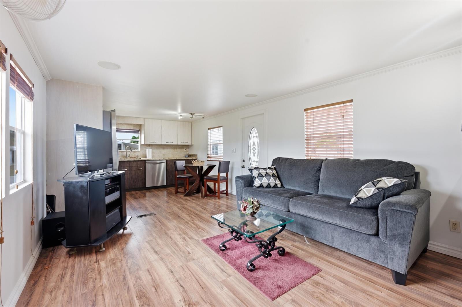 A living room with wood-look flooring, a gray sofa, and an open-concept kitchen — 12375 S Military Trail # 188, Boynton Beach FL 33436, BOYNTON BEACH, FL