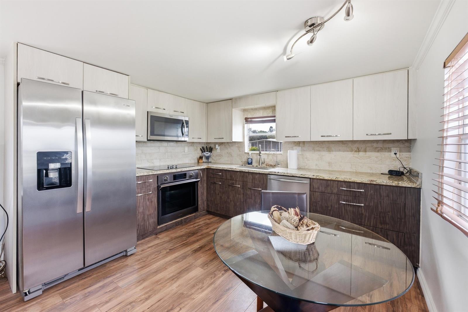 A kitchen features two-tone cabinetry, stainless steel appliances, granite countertops, and a glass dining table — 12375 S Military Trail # 188, Boynton Beach FL 33436, BOYNTON BEACH, FL