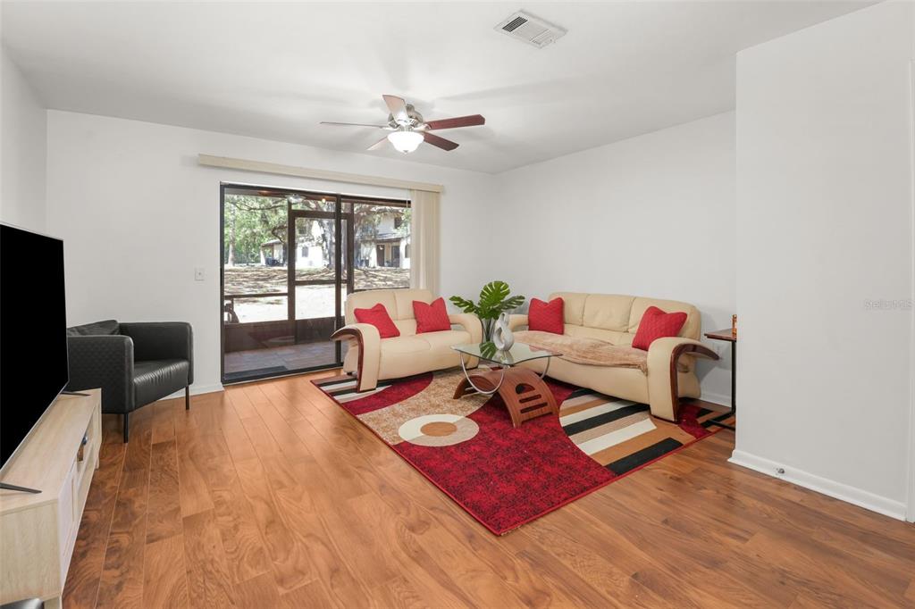A living room features light-colored sofas, a patterned red rug, and a sliding glass door — 2735 SW 35TH PLACE UNIT 903, GAINESVILLE, FL