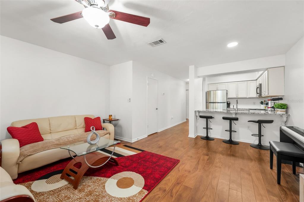 A living room with wood-look flooring, a beige sofa, and an open kitchen with bar seating — 2735 SW 35TH PLACE UNIT 903, GAINESVILLE, FL