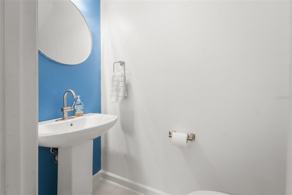 A half bathroom features a pedestal sink, a blue accent wall, and a round mirror — 2735 SW 35TH PLACE UNIT 903, GAINESVILLE, FL