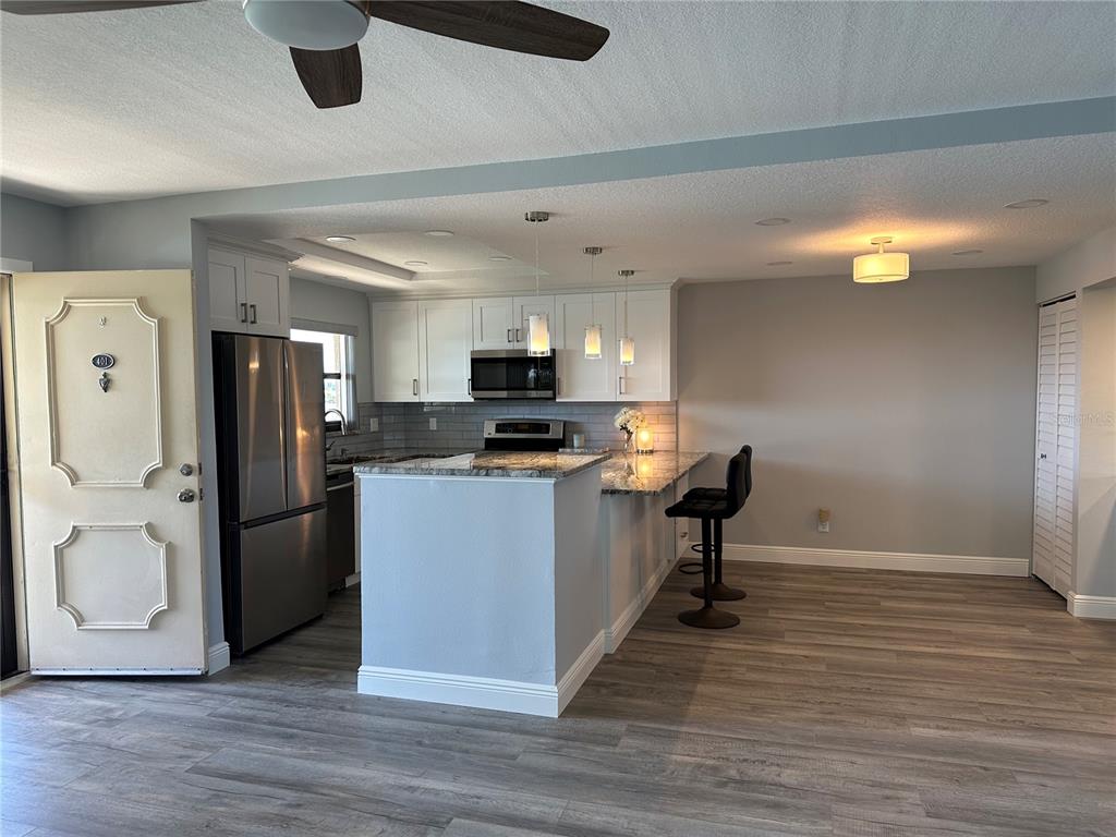 A kitchen with white cabinets, stainless steel appliances, and a granite-topped island with bar stools — 12500 CAPRI CIR N UNIT 401, TREASURE ISLAND, FL