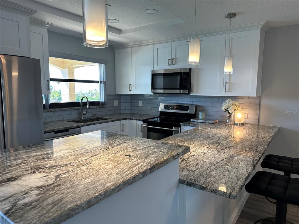 A kitchen features white cabinets, granite countertops, stainless steel appliances, and a gray subway tile backsplash — 12500 CAPRI CIR N UNIT 401, TREASURE ISLAND, FL