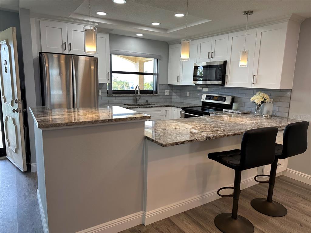 A kitchen features white cabinets, granite countertops, stainless steel appliances, and two black bar stools — 12500 CAPRI CIR N UNIT 401, TREASURE ISLAND, FL