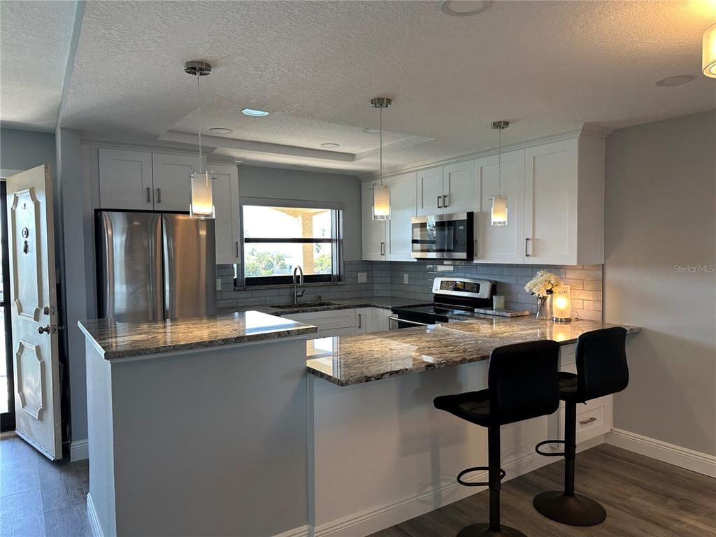 A kitchen features white cabinets, granite countertops, stainless steel appliances, and a breakfast bar — 12500 CAPRI CIR N UNIT 401, TREASURE ISLAND, FL