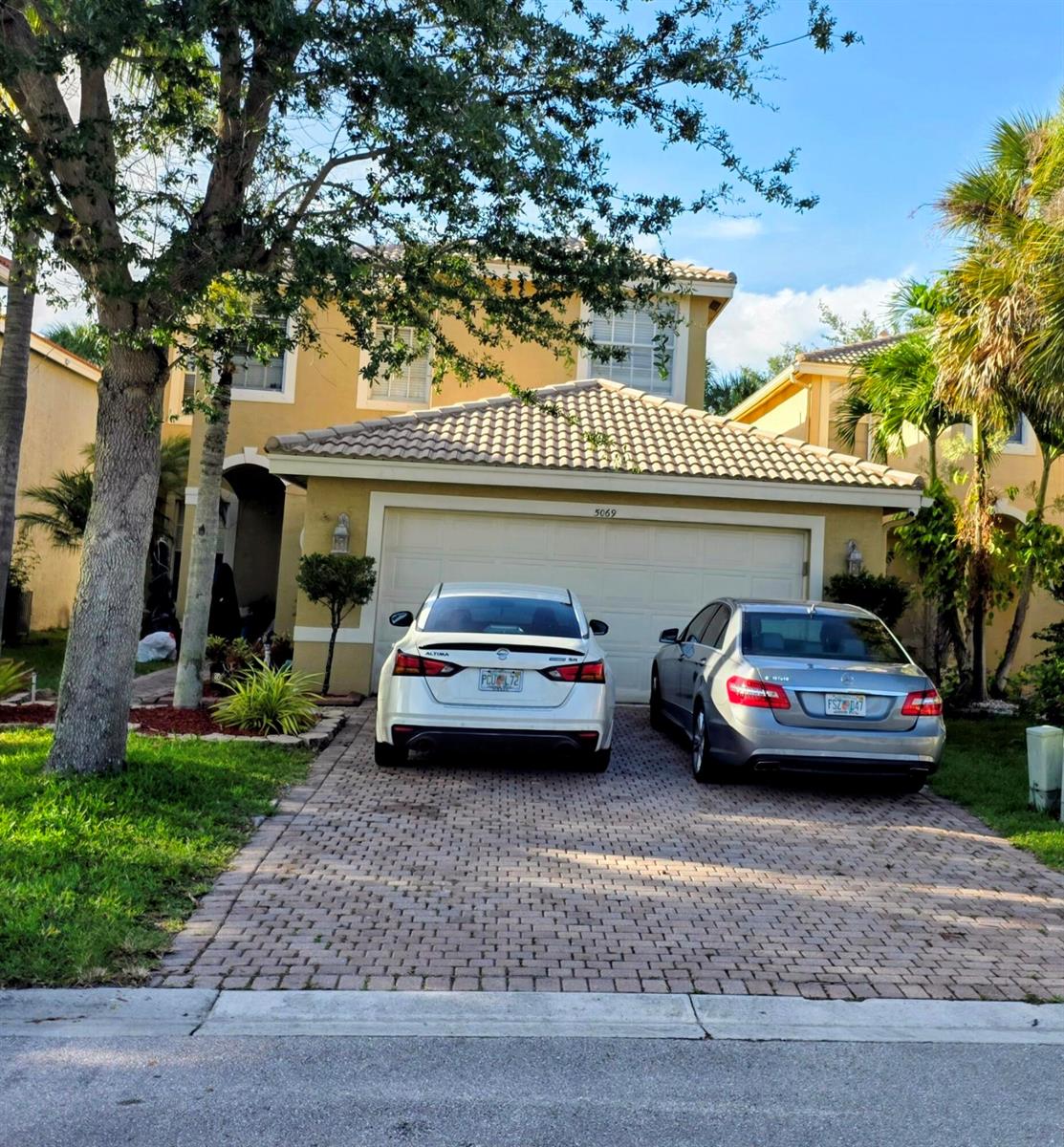 A two-story house with a tan exterior, a tiled roof, and two cars parked in the driveway — 5069 Starblaze Drive, FL 33463, FL