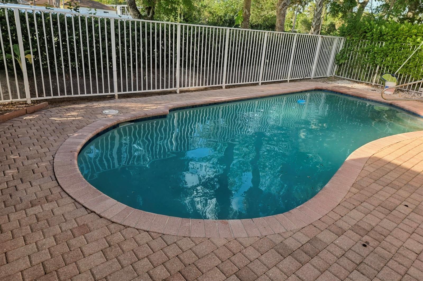 A kidney-shaped swimming pool with a brick paver deck is enclosed by a white fence — 5069 Starblaze Drive, FL 33463, FL