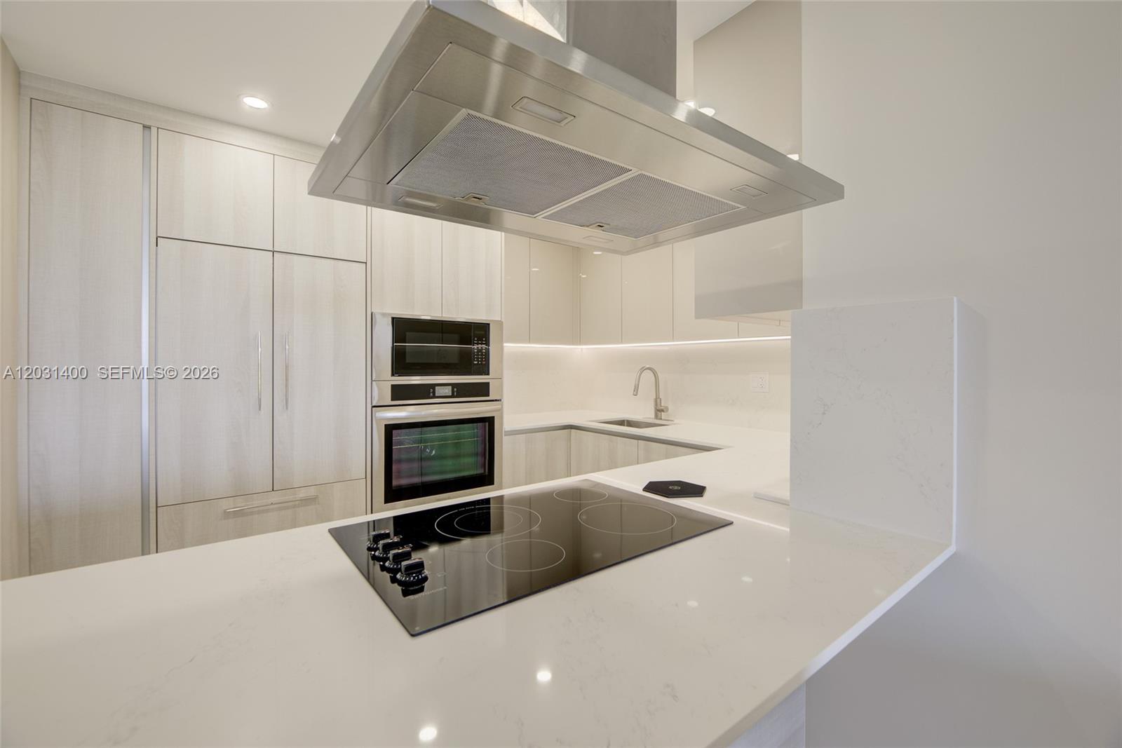 A modern kitchen features white quartz countertops, light wood cabinetry, and a stainless steel range hood — 600 Three Islands Blvd # 403, Hallandale Beach FL 33009, HALLANDALE BEACH, FL