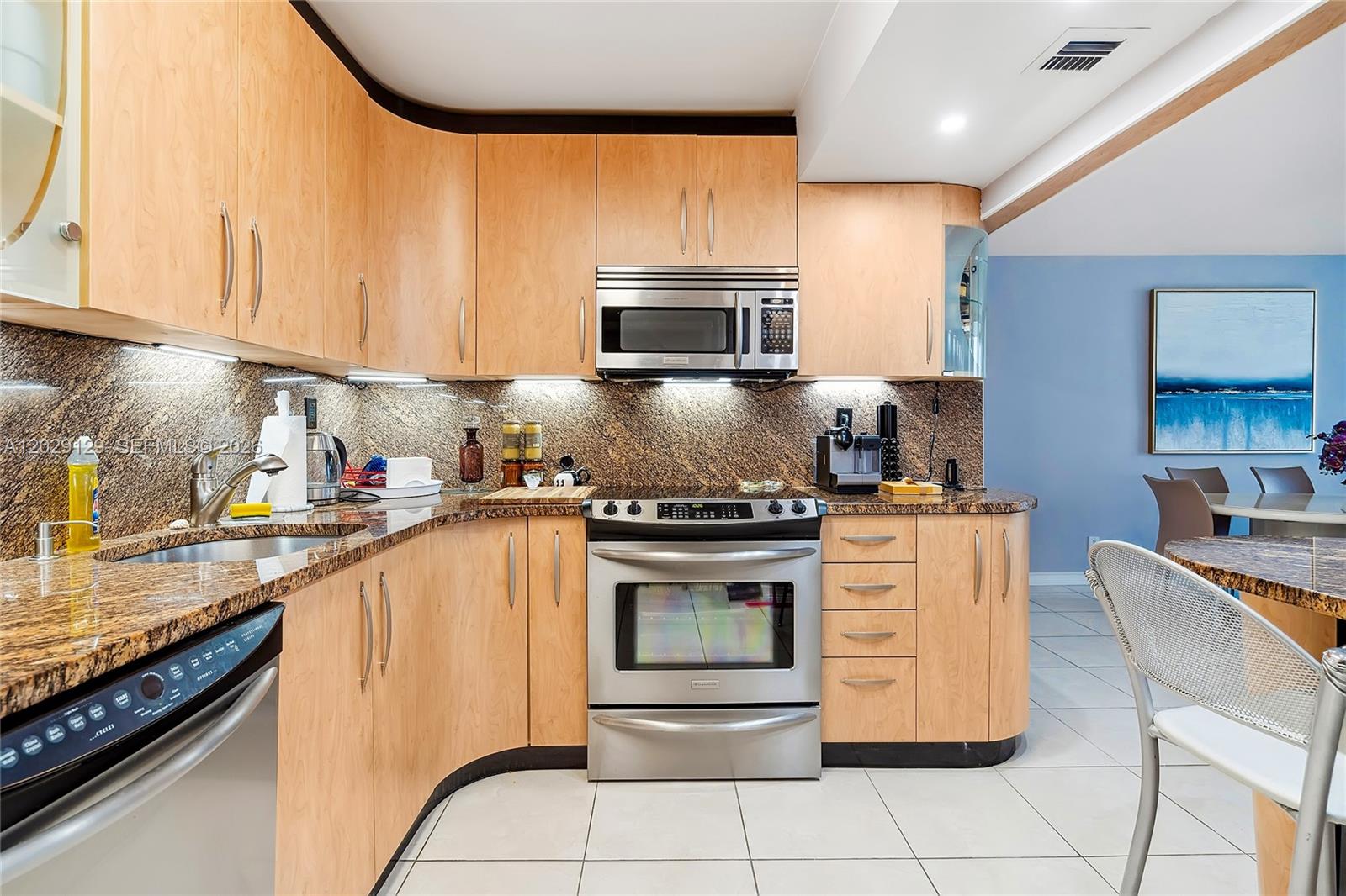 A kitchen features light wood cabinets, granite countertops, stainless steel appliances, and tile flooring — 1400 S Ocean Dr # 802, Hollywood FL 33019, HOLLYWOOD, FL