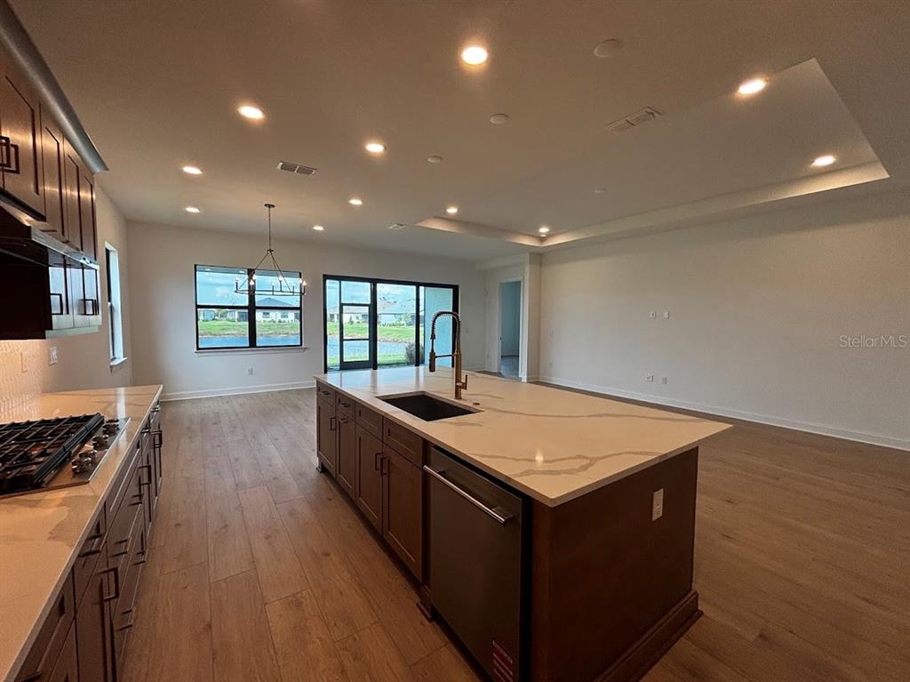 A modern kitchen features dark wood cabinets, a large quartz island, and light wood flooring — 5615 FREESTONE CIRCLE, APOLLO BEACH, FL