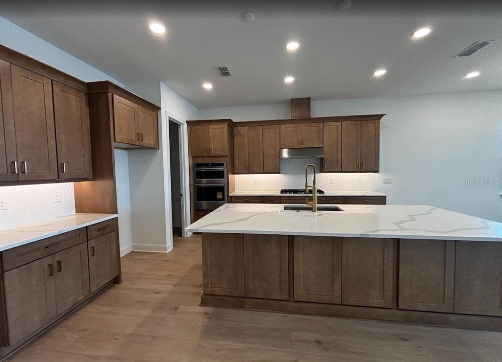 A kitchen features brown wood cabinets, a large white quartz island, and stainless steel appliances — 5615 FREESTONE CIRCLE, APOLLO BEACH, FL