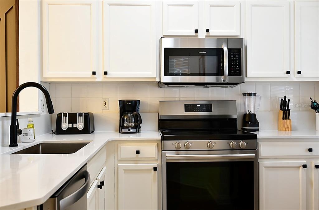 A kitchen features white cabinets, stainless steel appliances, a black faucet, and white countertops — 1043 PARK RIDGE CIRCLE, KISSIMMEE, FL
