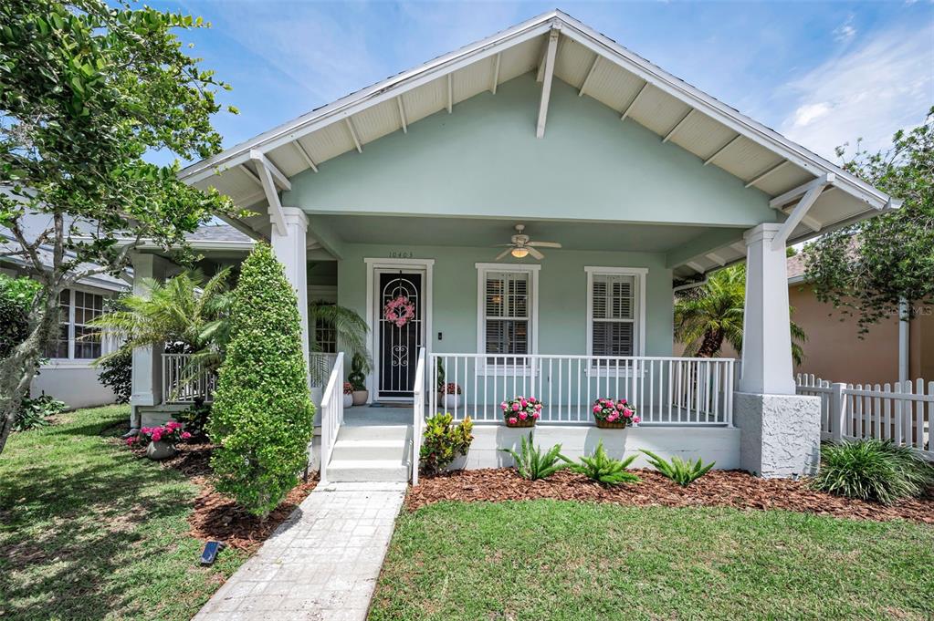 A light green bungalow features a covered front porch with white railings and columns — 10403 MICANOPY STREET, NEW PORT RICHEY, FL