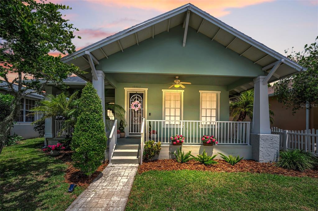 A light green bungalow features a covered front porch with white railings and a walkway — 10403 MICANOPY STREET, NEW PORT RICHEY, FL