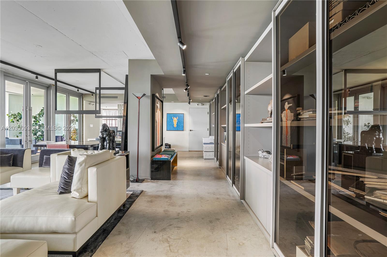 A modern living area features concrete floors, glass-fronted shelving, and a white sofa — 888 Biscayne Blvd, Miami FL 33132, MIAMI, FL
