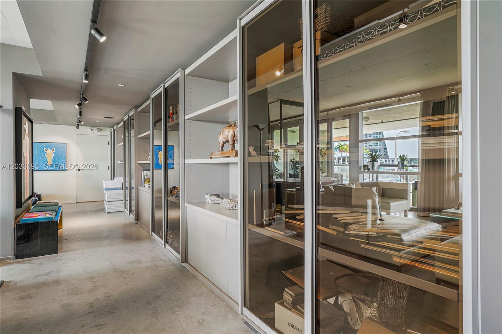 A hallway features glass-fronted display cabinets, concrete flooring, and track lighting along the ceiling — 888 Biscayne Blvd, Miami FL 33132, MIAMI, FL
