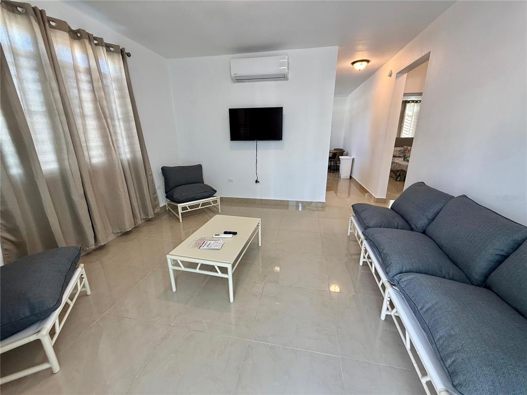 A living room with tile flooring, a sofa, a coffee table, and a wall-mounted television — Carr 115 km 8.7 CALLE HOSTOS, RINCON, PR
