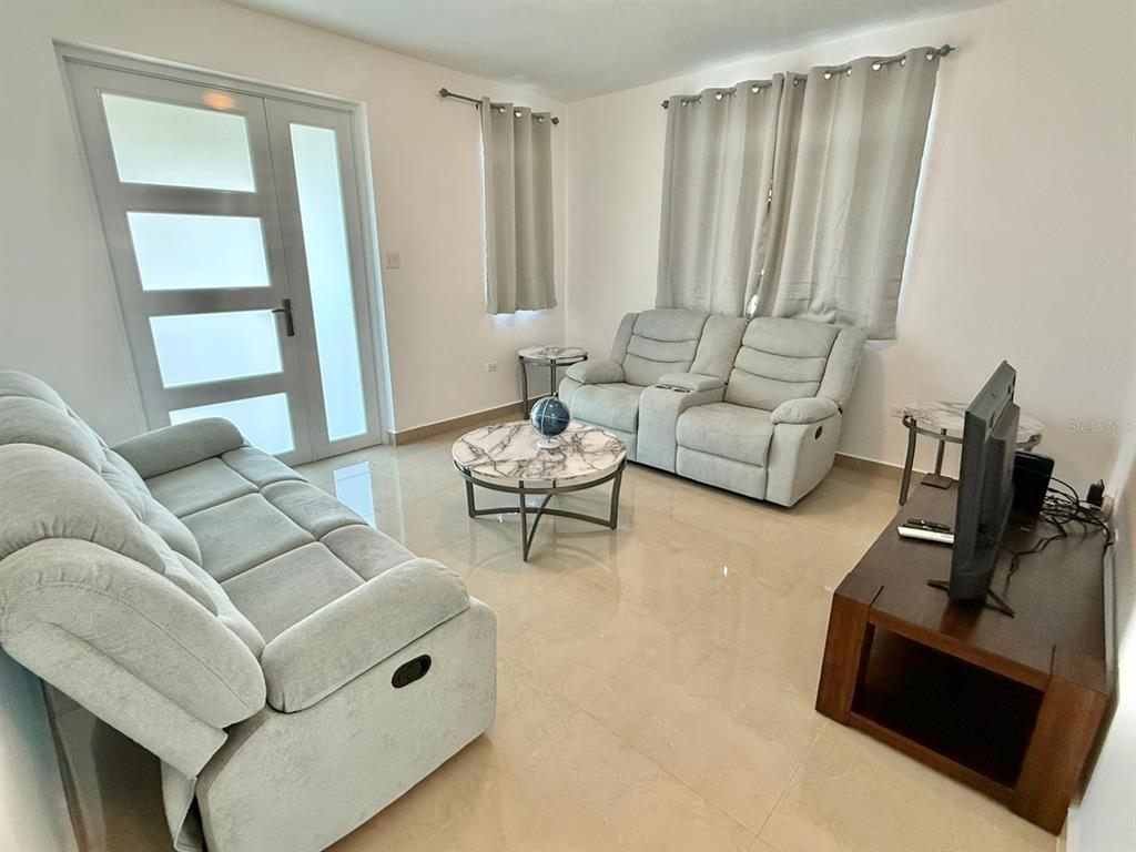 A living room features light-colored sofas, a marble-topped coffee table, and a television on a stand — Carr 115 km 8.7 CALLE HOSTOS, RINCON, PR