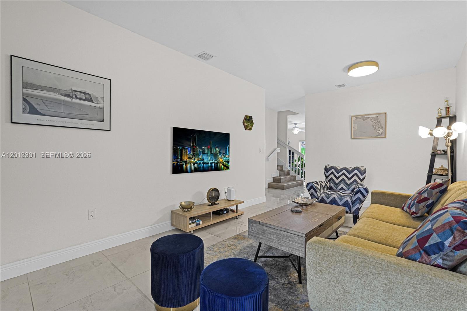 A living room features a mounted television, a sofa, patterned armchairs, and tile flooring — 9354 SW 220th St, Cutler Bay FL 33190, CUTLER BAY, FL