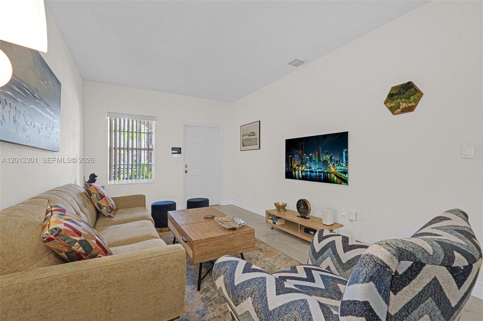 A living room features a beige sofa, a patterned armchair, and a wall-mounted television — 9354 SW 220th St, Cutler Bay FL 33190, CUTLER BAY, FL