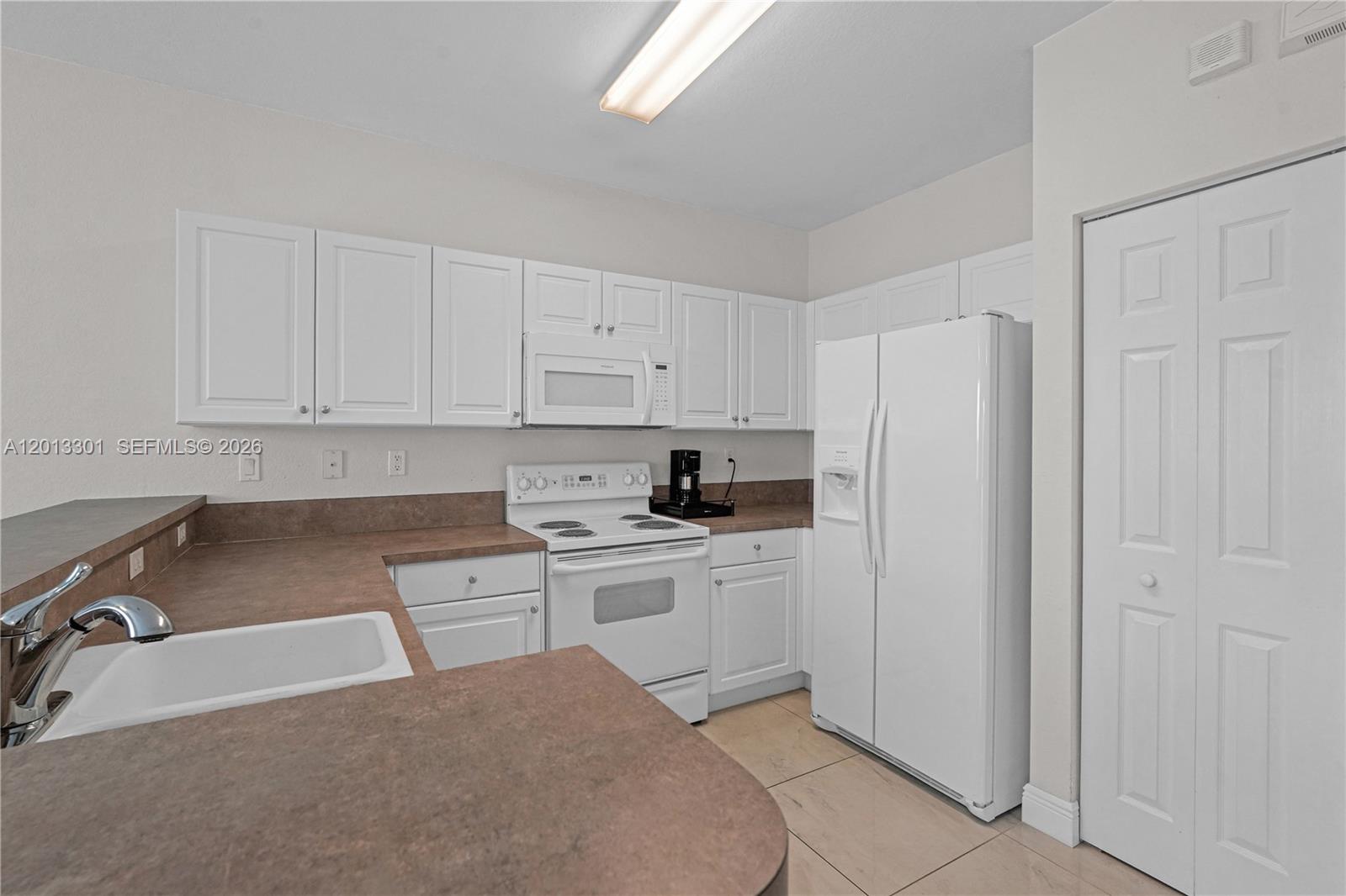 A kitchen features white cabinetry, white appliances, and brown countertops with a tile floor — 9354 SW 220th St, Cutler Bay FL 33190, CUTLER BAY, FL