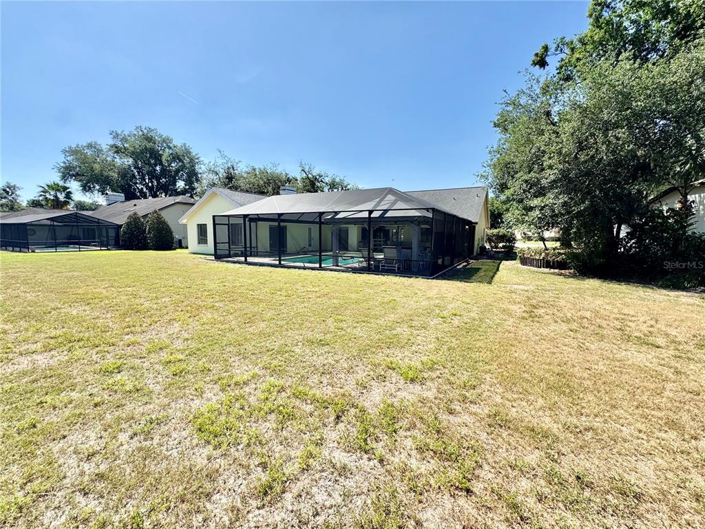 A backyard view of a house with a screened-in pool enclosure and a grassy lawn — 2804 WEDGEWOOD DRIVE, PLANT CITY, FL