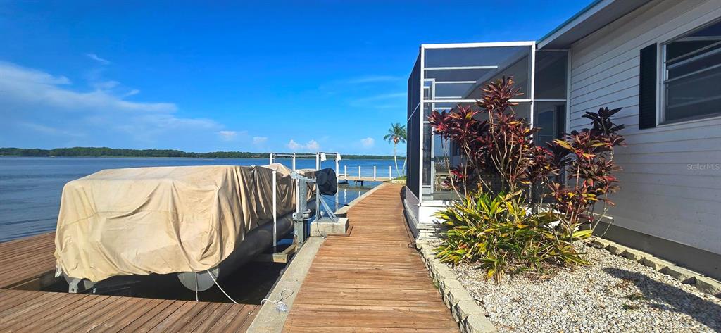 A wooden dock leads to a covered boat lift and a house with a screened porch — 271 COLONIAL BOULEVARD UNIT 11, PALM HARBOR, FL