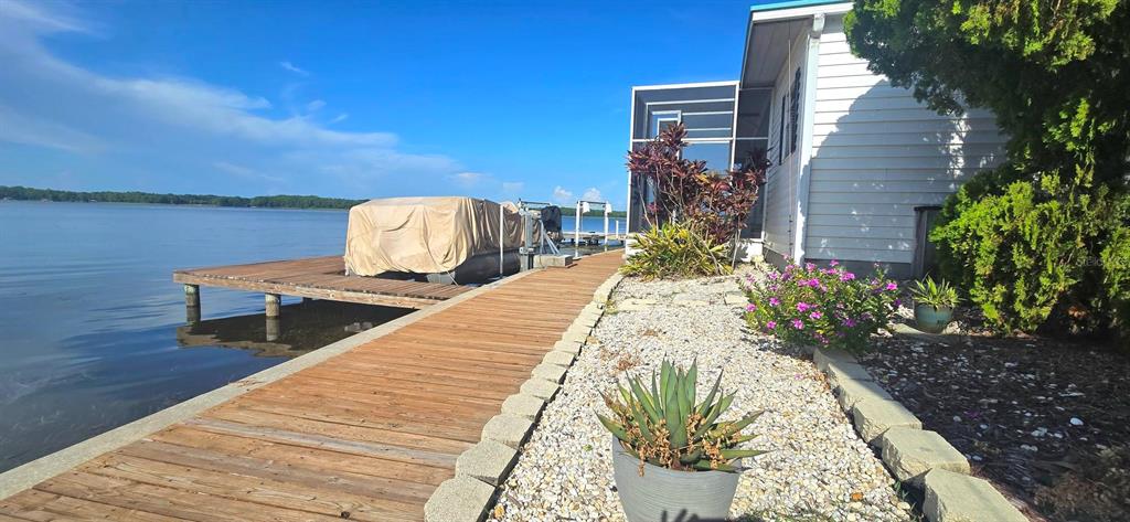 A wooden dock extends from a white house toward a lake with a covered boat — 271 COLONIAL BOULEVARD UNIT 11, PALM HARBOR, FL