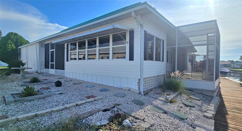 A white mobile home exterior features a screened-in porch, gravel landscaping, and a wooden dock — 271 COLONIAL BOULEVARD UNIT 11, PALM HARBOR, FL