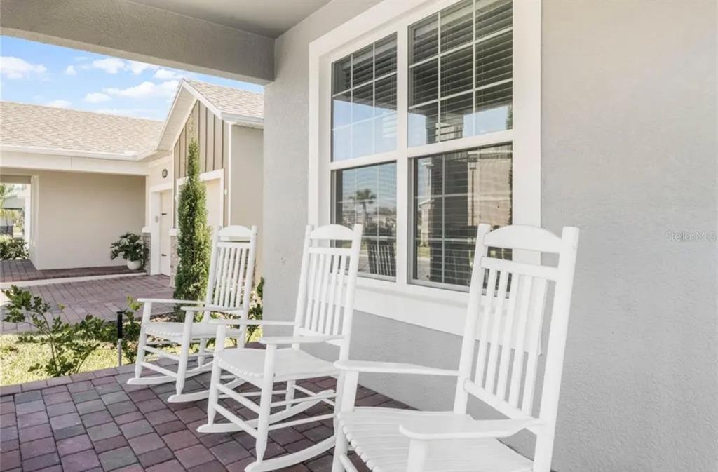Three white rocking chairs sit on a paved front porch in front of a window — 826 TERRAPIN DRIVE, DEBARY, FL