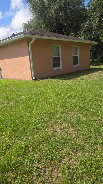 A side view of a tan, single-story house with two windows and a white downspout — 202 CHADWORTH DRIVE, KISSIMMEE, FL