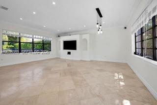 A bright living room features large windows, light tile flooring, and a central media wall — 712 Cremona Ave, Coral Gables FL 33146, CORAL GABLES, FL