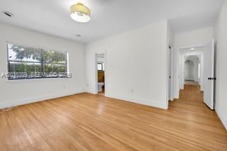 An empty room with light wood flooring, white walls, a window, and two doorways — 712 Cremona Ave, Coral Gables FL 33146, CORAL GABLES, FL