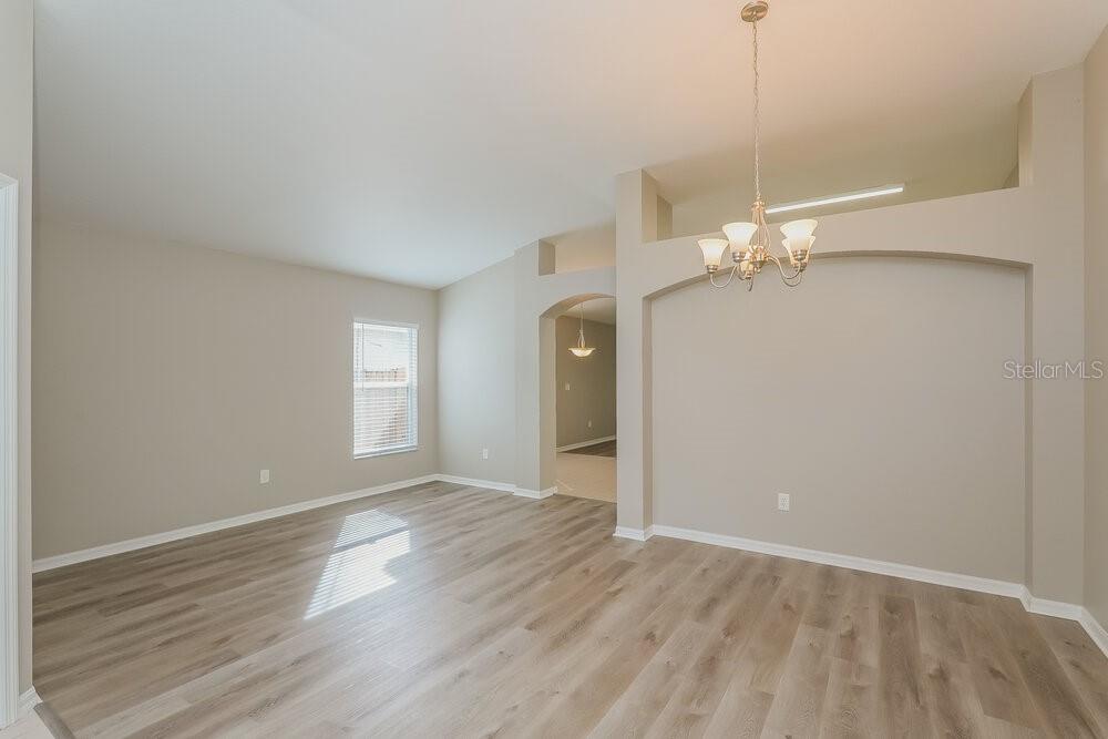 An empty dining room features light-colored wood-look flooring, beige walls, and a decorative chandelier — 411 SAND RIDGE DRIVE, VALRICO, FL