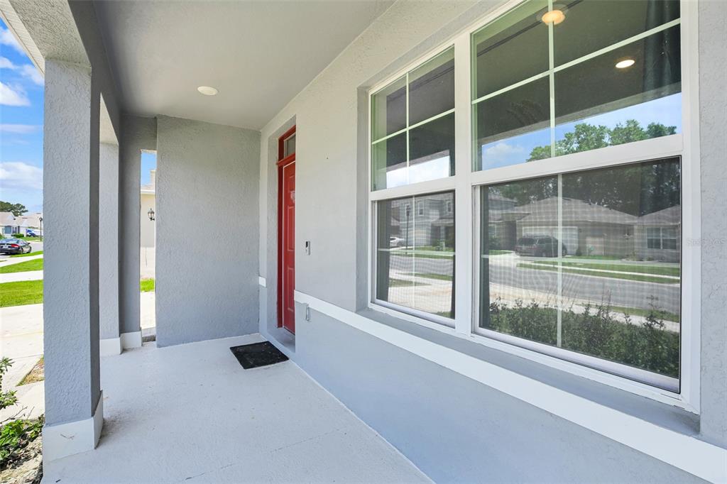 A covered front porch with a red door and large windows on a gray house — 11338 AMBER RIDGE DRIVE, ZELLWOOD, FL