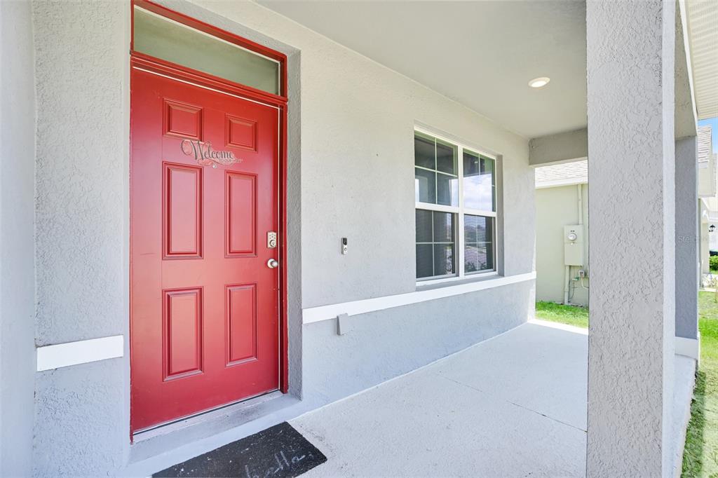 A red front door with a transom window sits on a covered concrete porch — 11338 AMBER RIDGE DRIVE, ZELLWOOD, FL