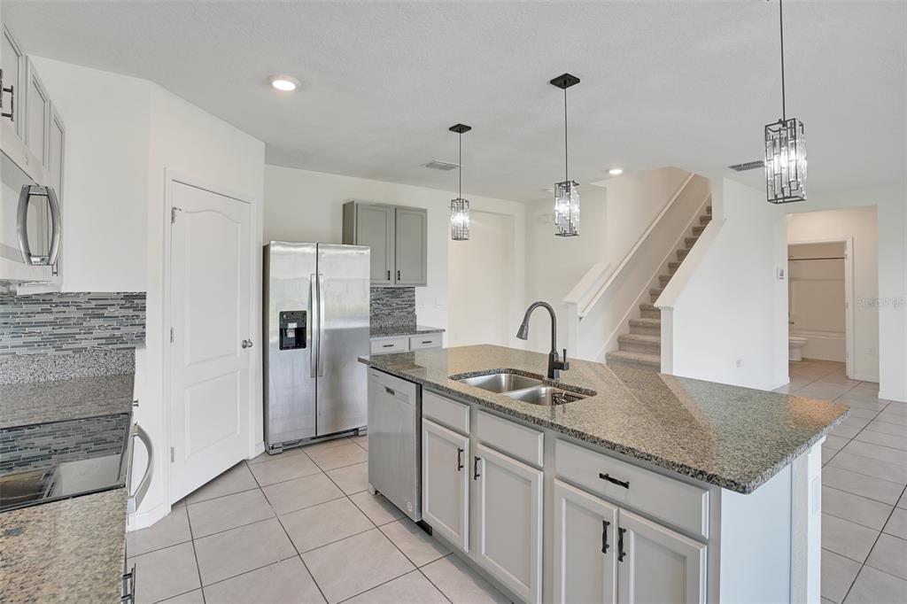 A kitchen with gray cabinets, granite countertops, stainless steel appliances, and an island with seating — 11338 AMBER RIDGE DRIVE, ZELLWOOD, FL