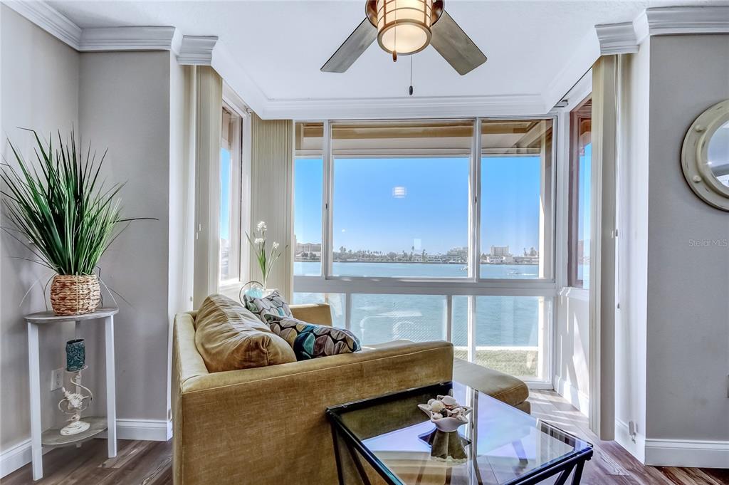 A sunroom with a sofa, glass coffee table, and large windows overlooking a bay — 644 ISLAND WAY UNIT 101, CLEARWATER BEACH, FL