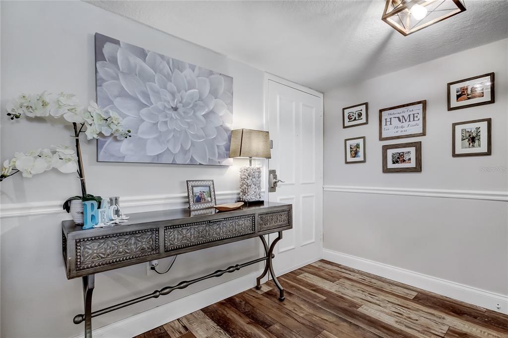 An entryway features a metal console table, a large floral canvas, and a gallery wall — 644 ISLAND WAY UNIT 101, CLEARWATER BEACH, FL