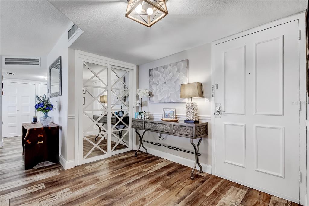 An entryway features wood-look flooring, a mirrored closet, a console table, and a white door — 644 ISLAND WAY UNIT 101, CLEARWATER BEACH, FL