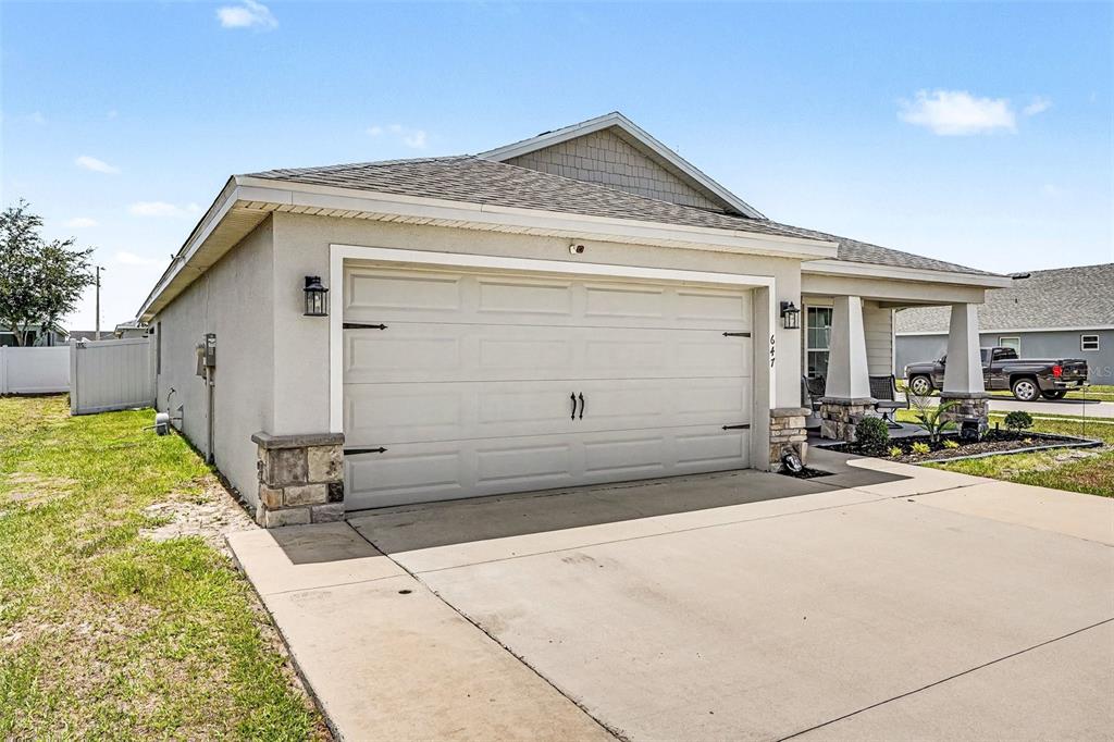 A beige single-story house features a two-car garage, stone accents, and a covered front porch — 647 LORIENT DRIVE, EAGLE LAKE, FL