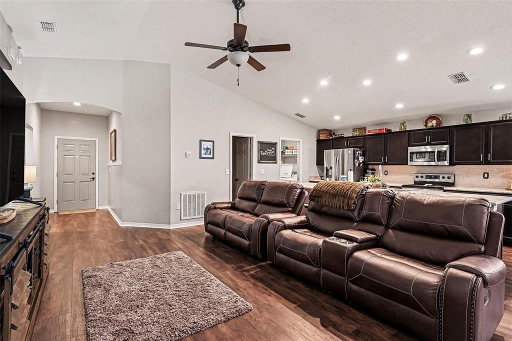 An open-concept living room features dark leather reclining sofas, wood-look flooring, and a kitchen area — 647 LORIENT DRIVE, EAGLE LAKE, FL