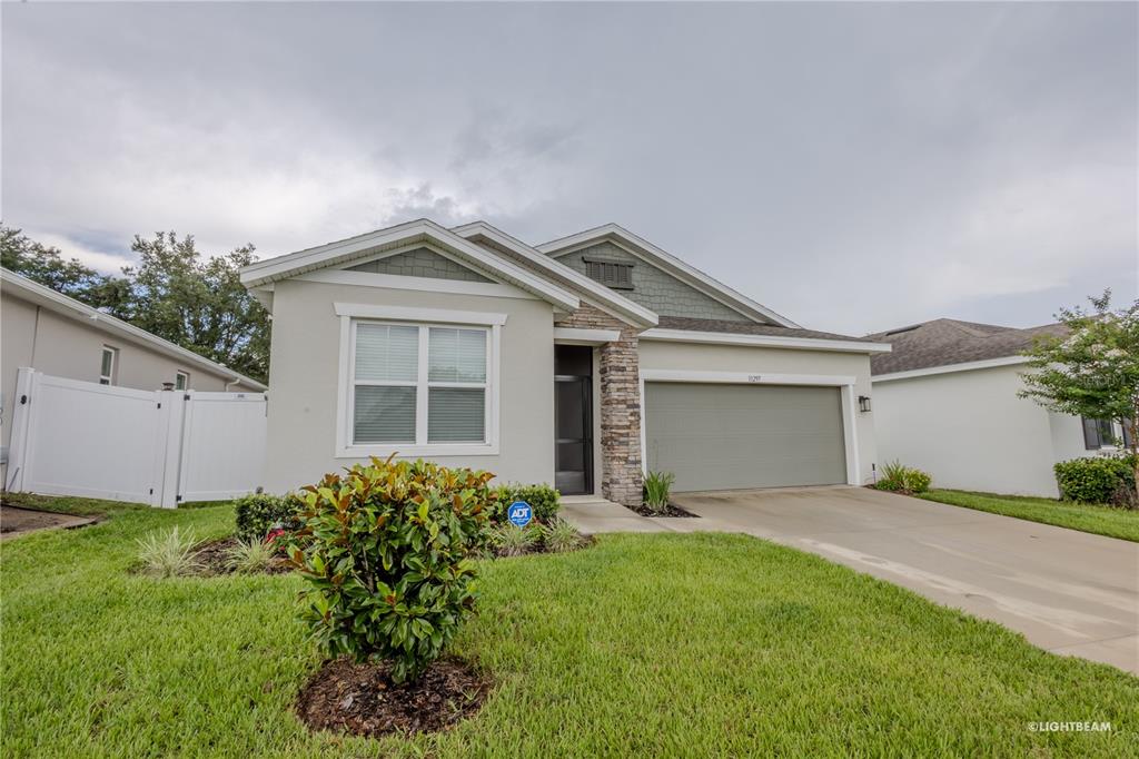 A single-story house with a beige stucco exterior, stone accents, and a two-car garage — 10297 CHURCH HAMMOCK ROAD, LEESBURG, FL
