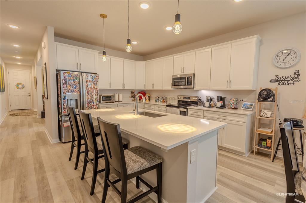 A modern kitchen features white cabinetry, a central island with bar seating, and stainless appliances — 10297 CHURCH HAMMOCK ROAD, LEESBURG, FL