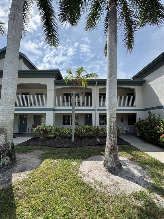 A two-story apartment building exterior features white balconies, palm trees, and a landscaped garden — 4457 W 45TH AVENUE UNIT 211, BRADENTON, FL