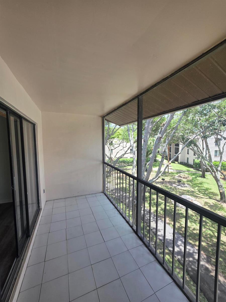 A screened-in balcony with white tile flooring overlooks a grassy area with trees — 202 Foxtail Drive # F3, FL 33415, FL