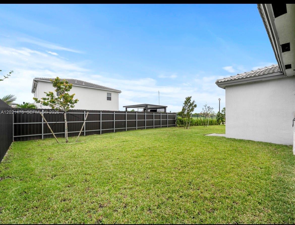 A grassy backyard features a dark metal fence and a young tree — 14884 SW 162nd St, Miami FL 33187, MIAMI, FL