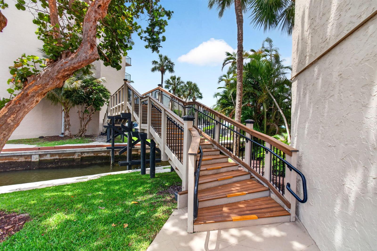A wooden pedestrian bridge with black railings spans a canal next to a building — 12 Royal Palm Way # 501, Boca Raton FL 33432, BOCA RATON, FL