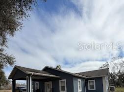 A dark blue single-story house with a carport under a cloudy sky — 7040 LUMBERTON ROAD, ZEPHYRHILLS, FL