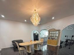 A dining room features a crystal chandelier, a long table, and dark tiled flooring — 7040 LUMBERTON ROAD, ZEPHYRHILLS, FL